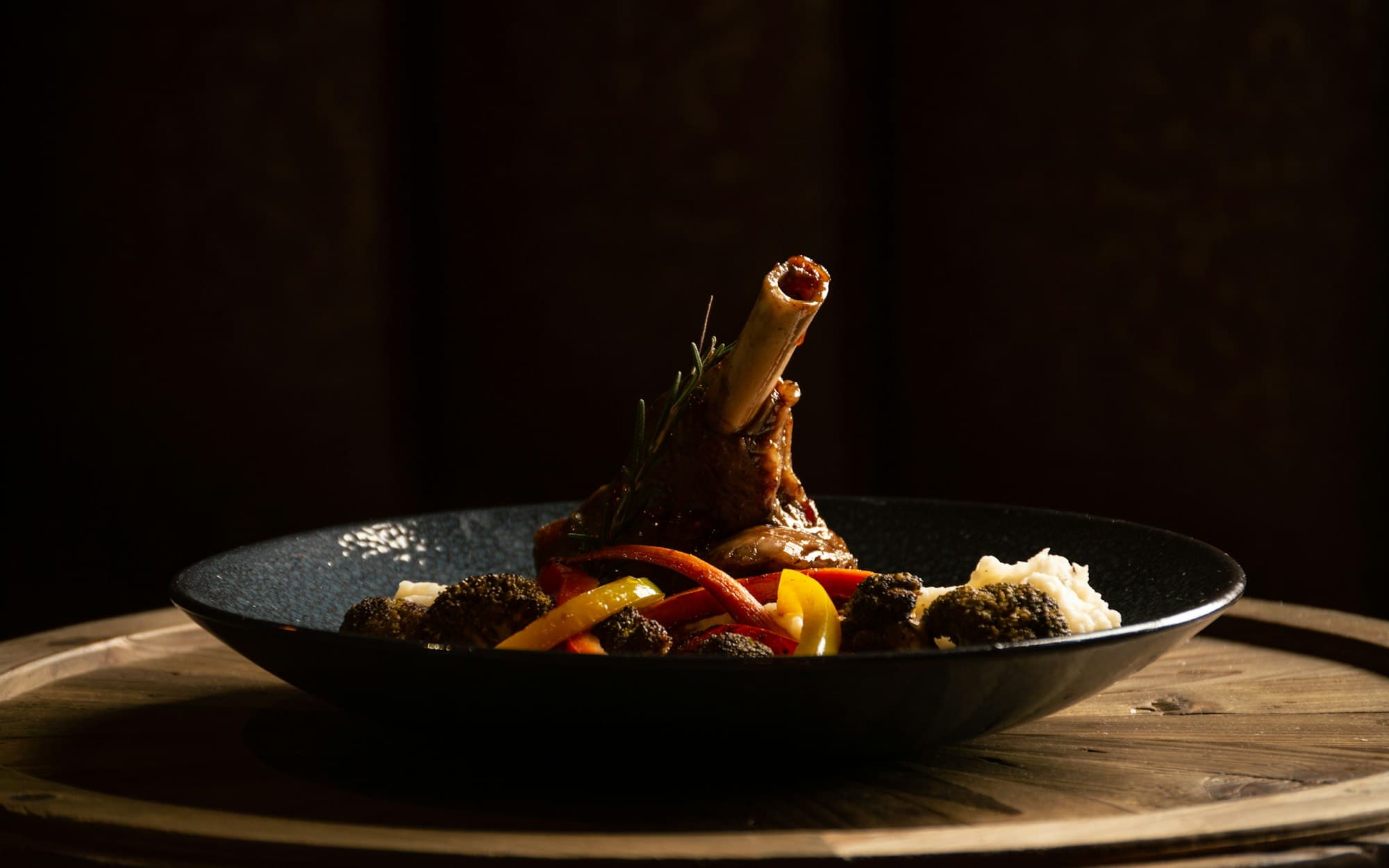 A slow-cooked lamb shank plated in a dark pan under low restaurant light